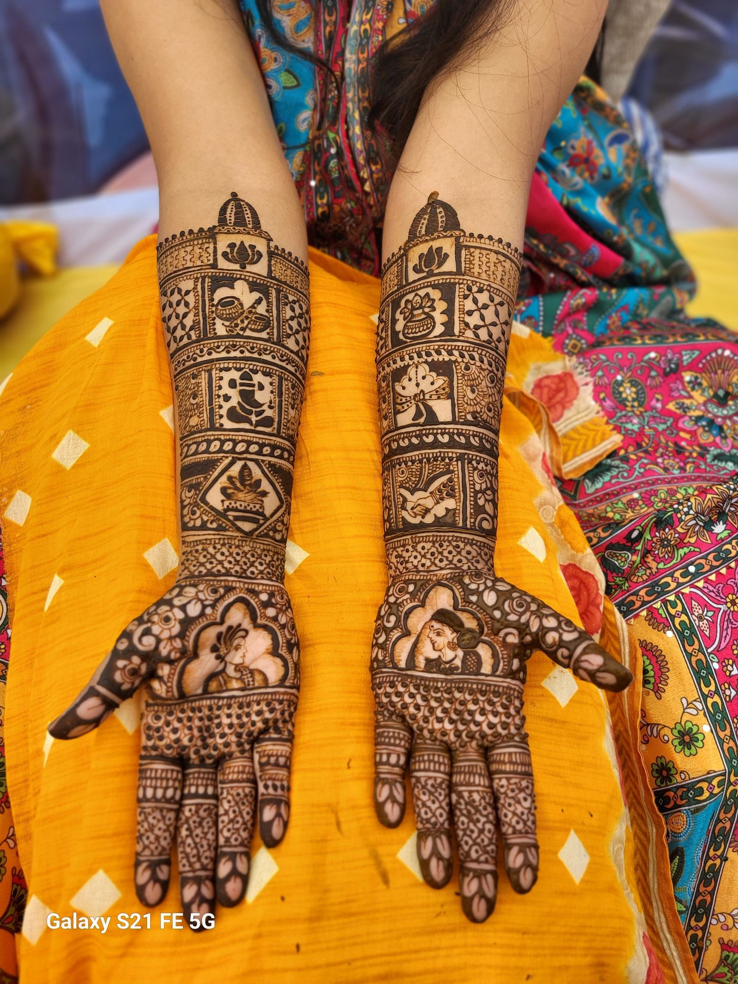 Intricate henna designs on both arms, featuring floral and geometric patterns on a colorful background.